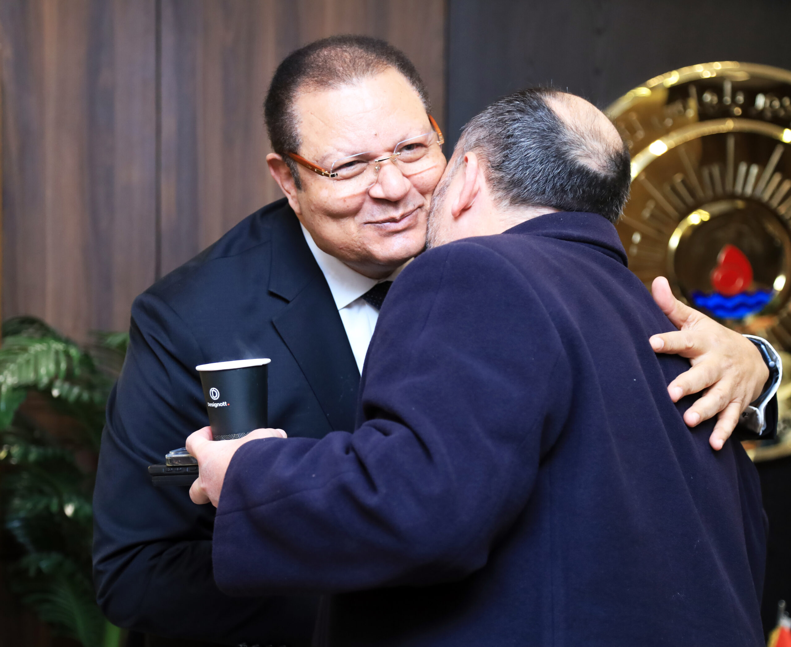 Two VIPs greeting each other during a Designott-managed conference, one holding a branded cup